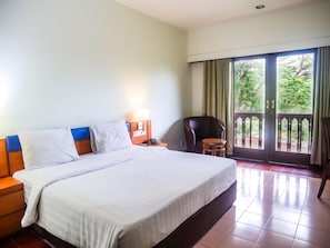 A hotel room with a large bed, a nightstand, a chair, and a view of the outdoors through a sliding door.