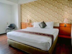 A hotel room with a large bed, a nightstand, a chair, and a patterned wall.