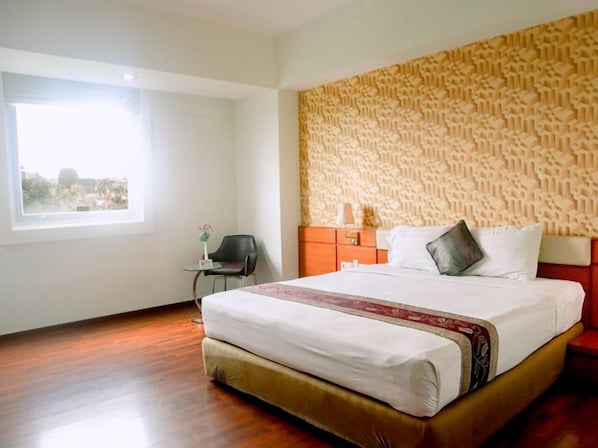 A hotel room with a large bed, a window, a chair, and a patterned wall.