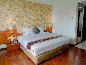 A neatly made bed with a patterned headboard, wooden nightstands with lamps, and a wooden floor.