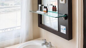 A bathroom with a white sink, a mirror, and a window with sheer curtains.