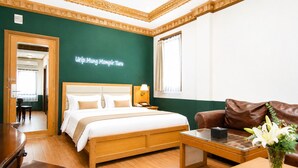 A hotel room with a bed, a desk, a brown leather sofa, a vase with flowers, and a green accent wall.