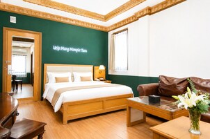 Habitación de hotel con cama, escritorio, sofá de cuero marrón, un jarrón con flores y una pared de acento verde.