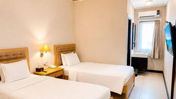 Une chambre d’hôtel avec deux lits, une table de chevet avec une lampe, une petite salle de bain et un téléviseur fixé au mur.