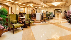 A spacious lobby with a checkered floor, green upholstered chairs, a reception desk, and a chandelier.