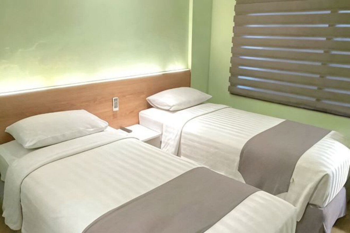 A room with two beds, a wooden headboard, and a window with blinds.