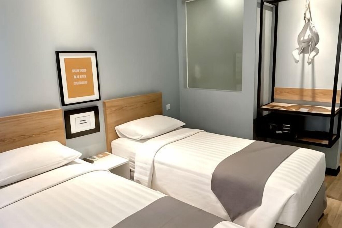 Habitación de hotel con dos camas, cabecero de madera, un cuadro enmarcado en la pared y una lámpara colgante.