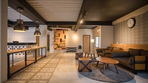 A modern living area with a sofa, coffee table, and pendant lights. There is a patterned floor and a clock on the wall. - Allstay Ecotel Yogyakarta (Depok)