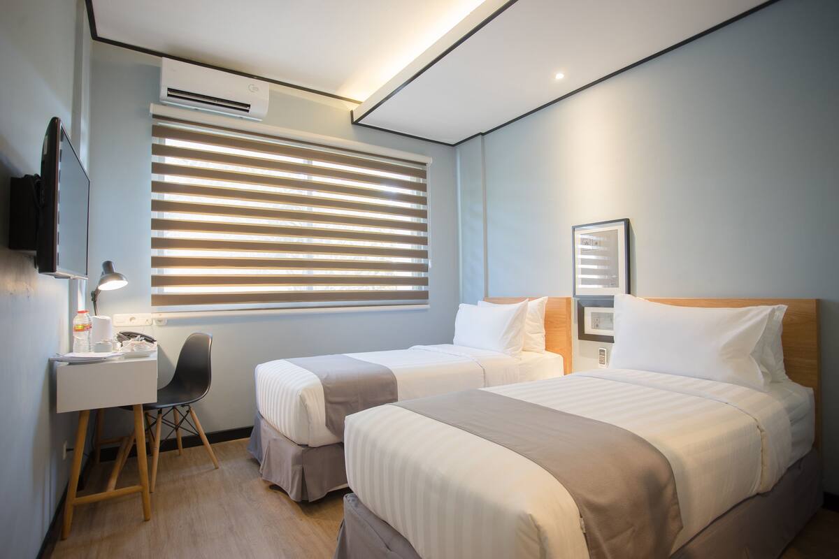 A hotel room with two beds, a desk, a chair, and a TV.