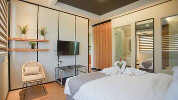 Ein modernes Hotelzimmer mit Bett, Fernseher, Sessel und Kleiderschrank.