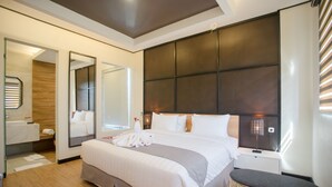 A modern hotel room with a large bed, a bedside table, a mirror, a wall-mounted light, and a wooden floor. - Allstay Ecotel Yogyakarta (Depok)