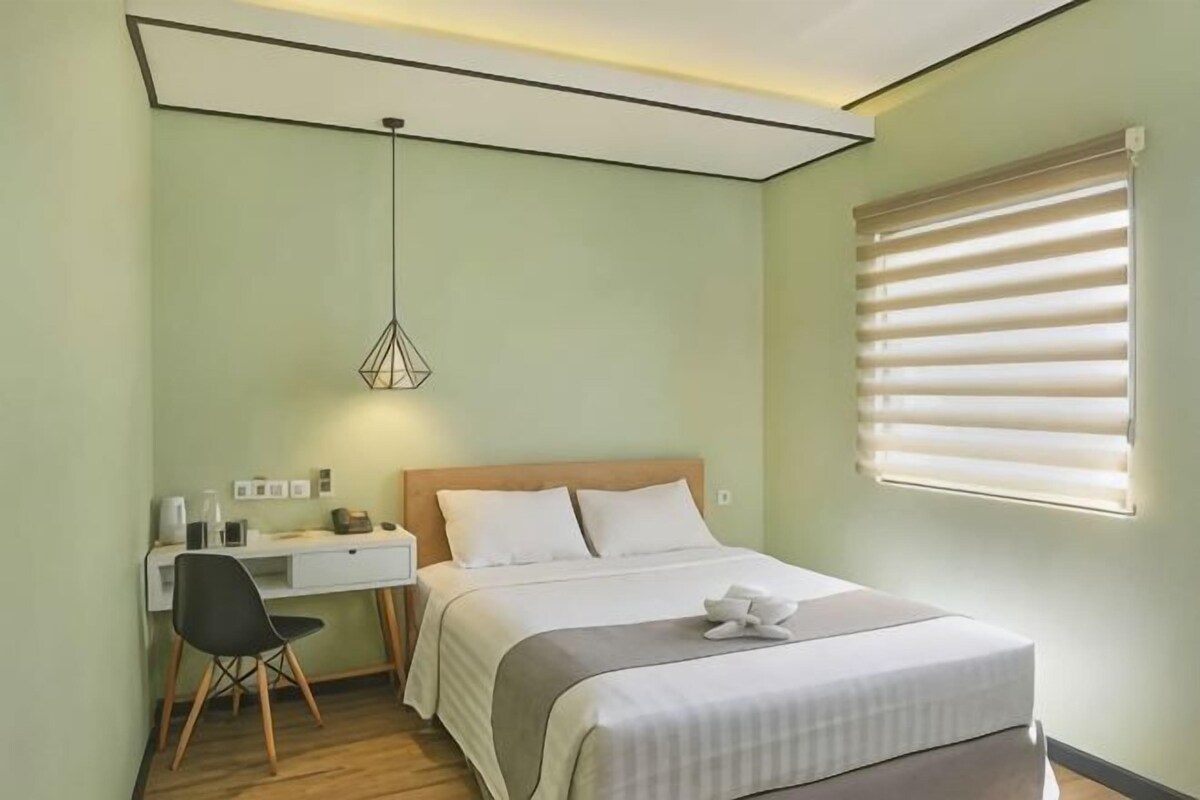 Un dormitorio con cama, mesita de noche, lámpara y ventana con persianas.