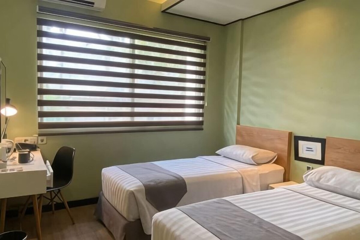 A room with two beds, a desk, a chair, and a window with blinds.