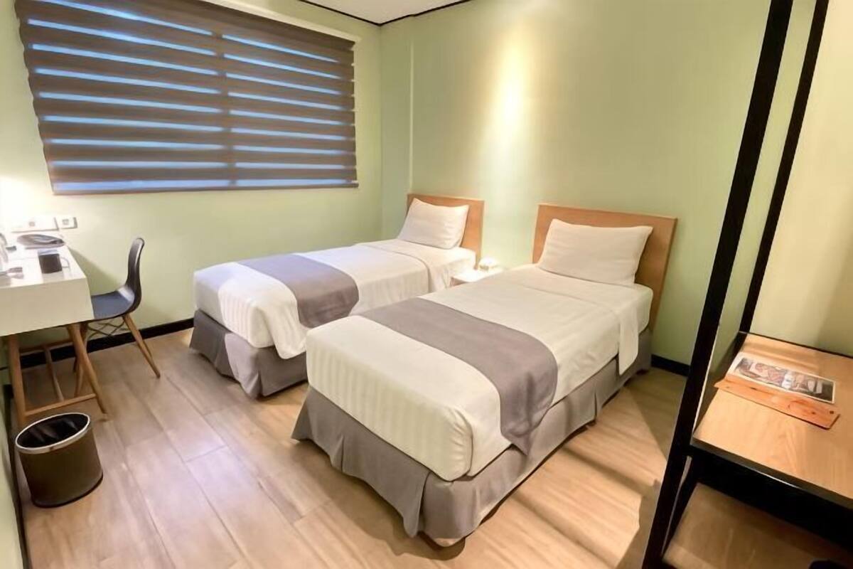 A twin room with two beds, a desk, a chair, and a window with blinds.