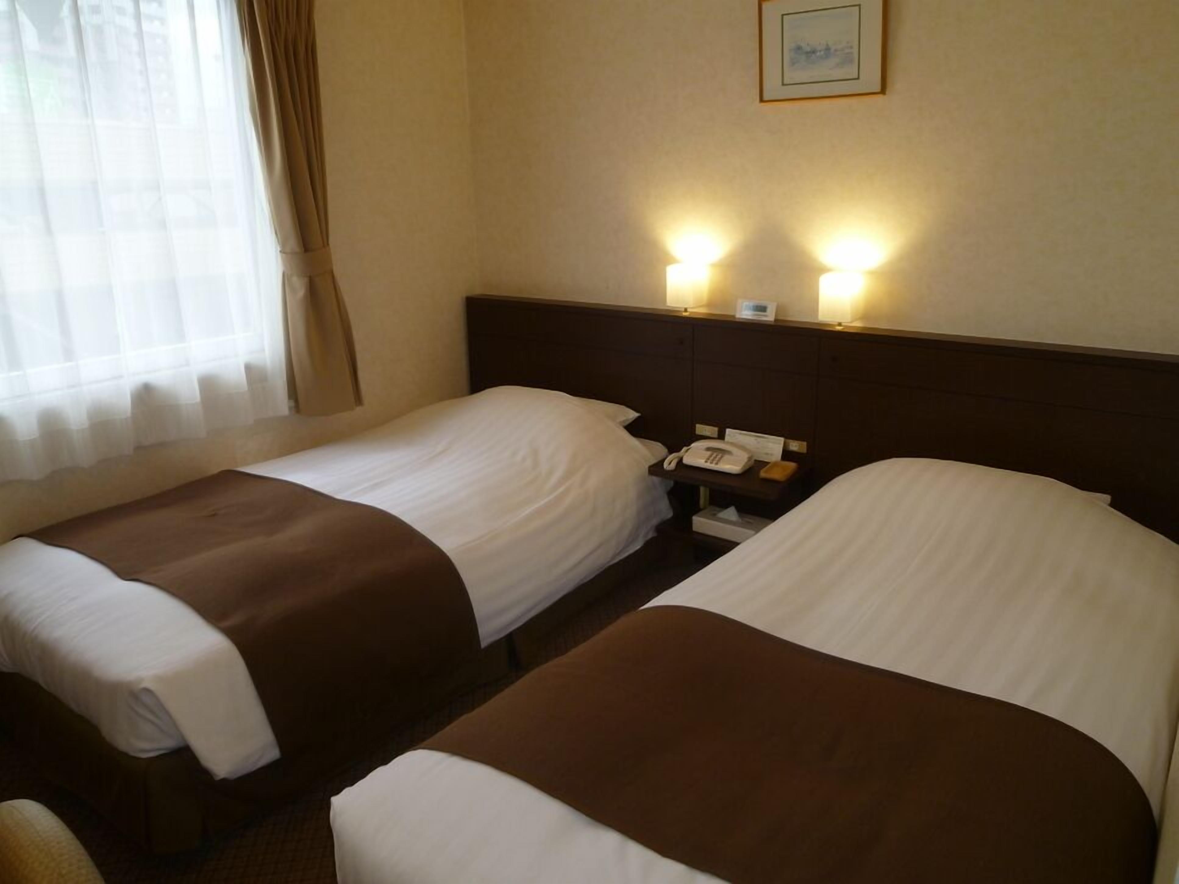 Ein Hotelzimmer mit zwei Einzelbetten, einem Nachttisch mit Telefon und einer Wandleuchte.