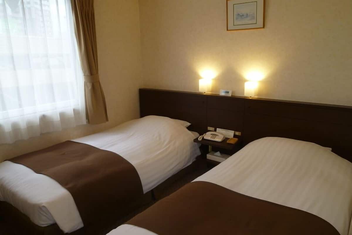 Ein Hotelzimmer mit zwei Einzelbetten, einem Nachttisch mit Telefon und einer Wandleuchte.