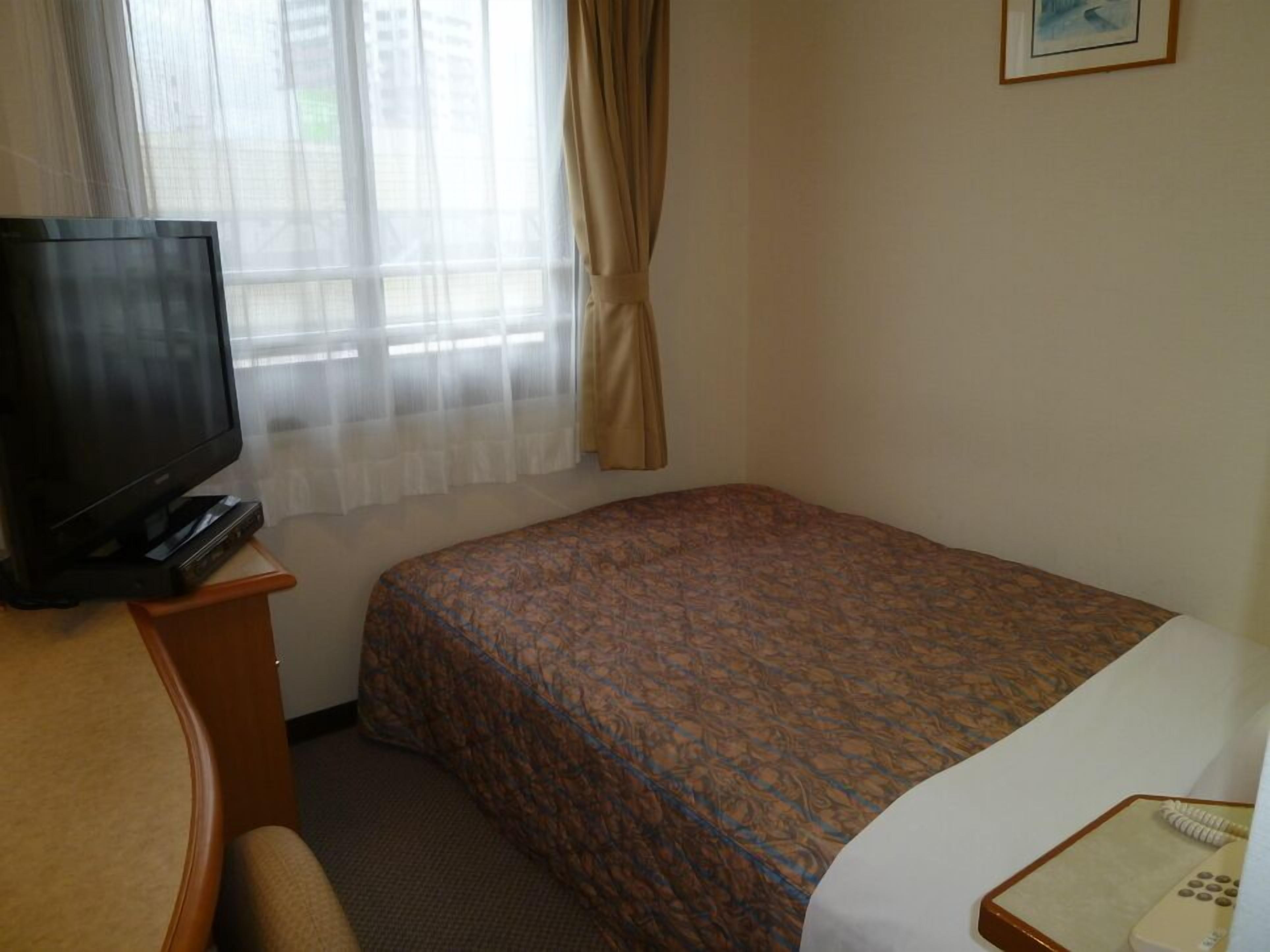 Ein Hotelzimmer mit einem Bett, einem Fernseher auf einem Tisch, einem Telefon und einem Fenster mit Vorhängen.