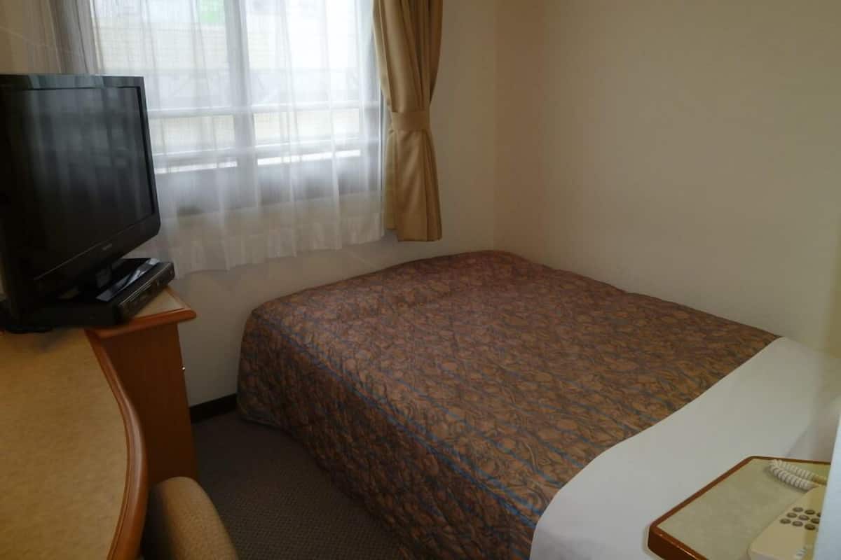 Ein Hotelzimmer mit einem Bett, einem Fernseher auf einem Tisch, einem Telefon und einem Fenster mit Vorhängen.