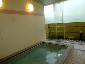 Zona de piscina con suelo de baldosas, separador de vidrio y valla de madera al fondo.
