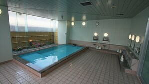 A swimming pool with a tiled floor, a shower area, and a mirror with lights.