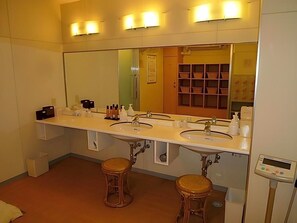 Un baño con tres lavamanos, un espejo grande y dos taburetes.