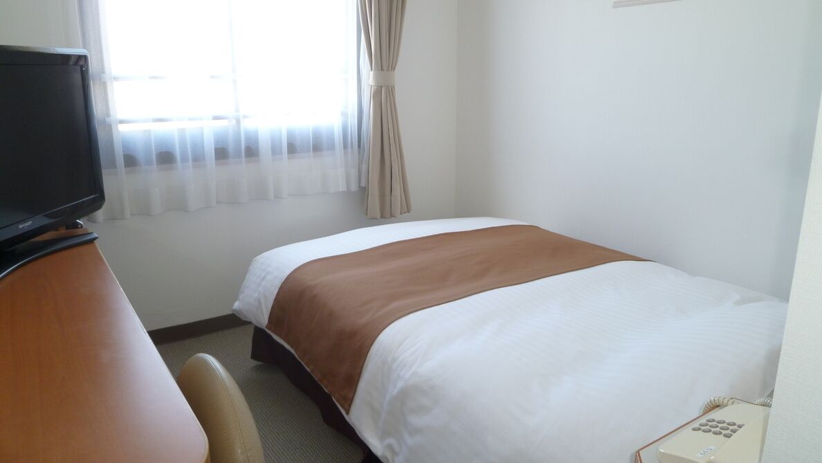 Ein Hotelzimmer mit Bett, Schreibtisch, Fernseher und Telefon.