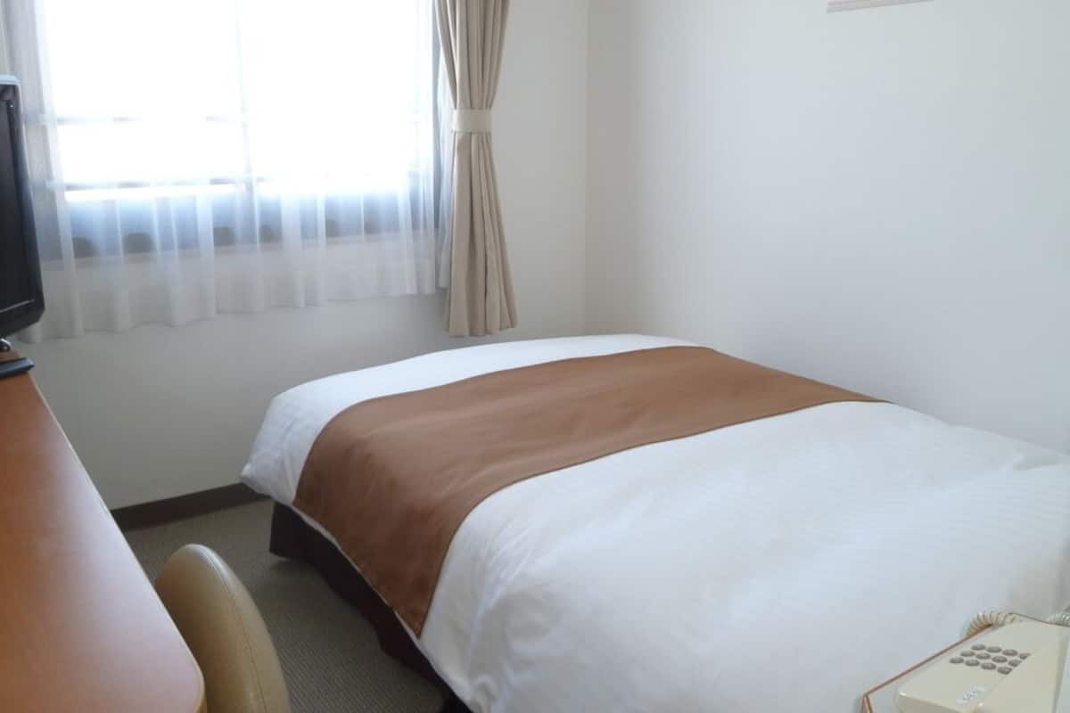 Ein Hotelzimmer mit Bett, Schreibtisch, Fernseher und Telefon.