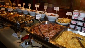 A buffet with various food items, including hot dogs and pasta, with labels in a foreign language.