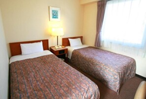 Una habitación de hotel con dos camas, una mesita de noche, una lámpara y un ventanal con cortinas.