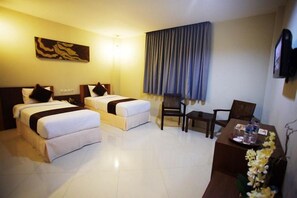 A hotel room with two beds, a desk, a chair, and a television.