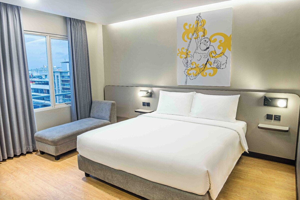 Une chambre d’hôtel avec un grand lit, un coin salon, une fenêtre avec des rideaux et une œuvre d’art accrochée au mur.