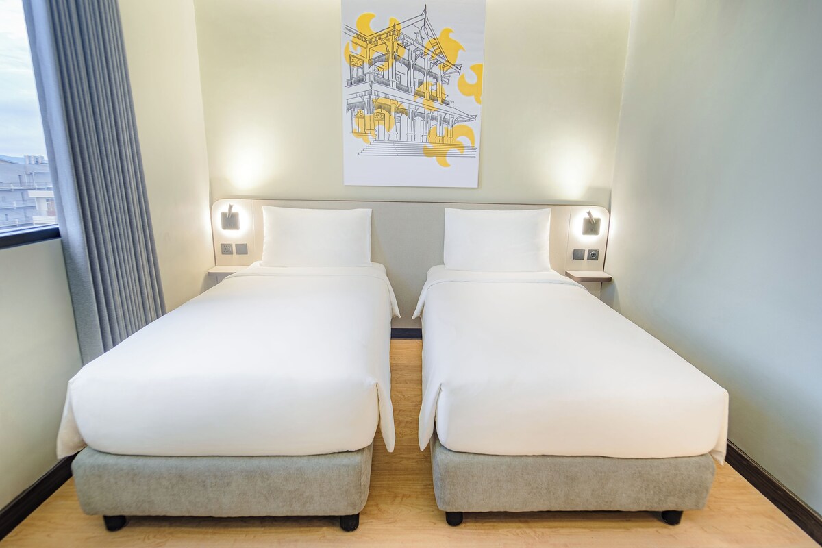Une chambre d’hôtel avec deux lits simples, une fenêtre avec des rideaux et une œuvre d’art accrochée au mur.