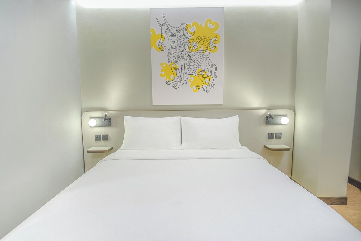 Une chambre d’hôtel comprenant un lit, deux tables de chevet, une lampe fixée au mur et un élément décoratif placé au-dessus du lit.