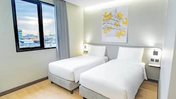 Habitación de hotel con dos camas, ventana con vistas a edificios, una obra de arte colgada en la pared y un interruptor de luz.