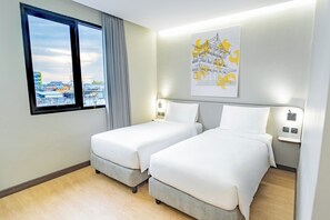 A hotel room with two beds, a window with a view of buildings, a wall-mounted artwork, and a light switch. - YELLO Hotel Samarinda (Samarinda)