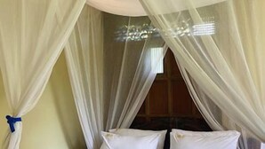 A bed with white linens, a white canopy, and a towel on the bed.