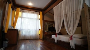 Une chambre avec un lit, des rideaux, une télévision et un plancher en bois.