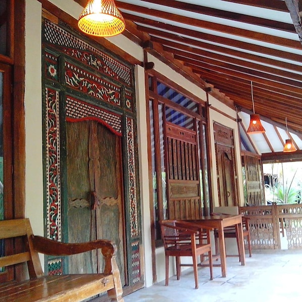 A traditional wooden structure with intricate carvings on the door and walls, a bench, and a table.