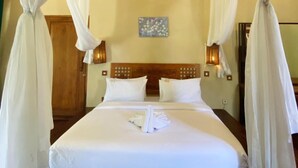 A hotel room with a four-poster bed, white bedding, and a canopy.