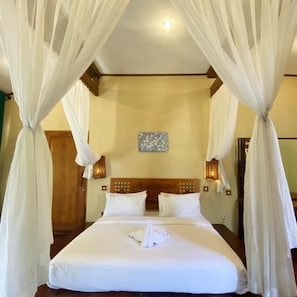 A hotel room with a four-poster bed, white bedding, and a canopy.