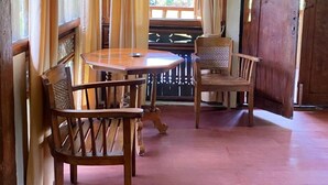 A wooden dining area with a round table and two chairs, a wooden door, and a window with curtains.