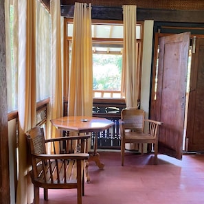 A wooden dining area with a round table and two chairs, a wooden door, and a window with curtains.