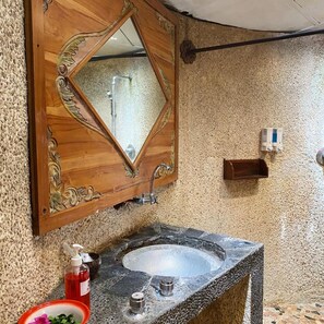 A bathroom with a wooden-framed mirror, a granite sink, a soap dispenser, and a towel rack.
