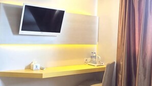 Habitación de hotel con televisión montada, escritorio con un teléfono y una taza, y una cortina.
