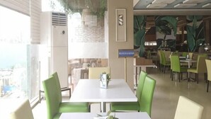 Un restaurante con mesas y sillas blancas, vistas a la ciudad y un mural tropical en la pared.