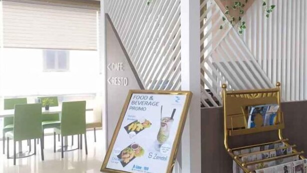 Un interior moderno con sillas verdes, un cartel promocional de comida y bebidas, y un atril dorado para revistas.
