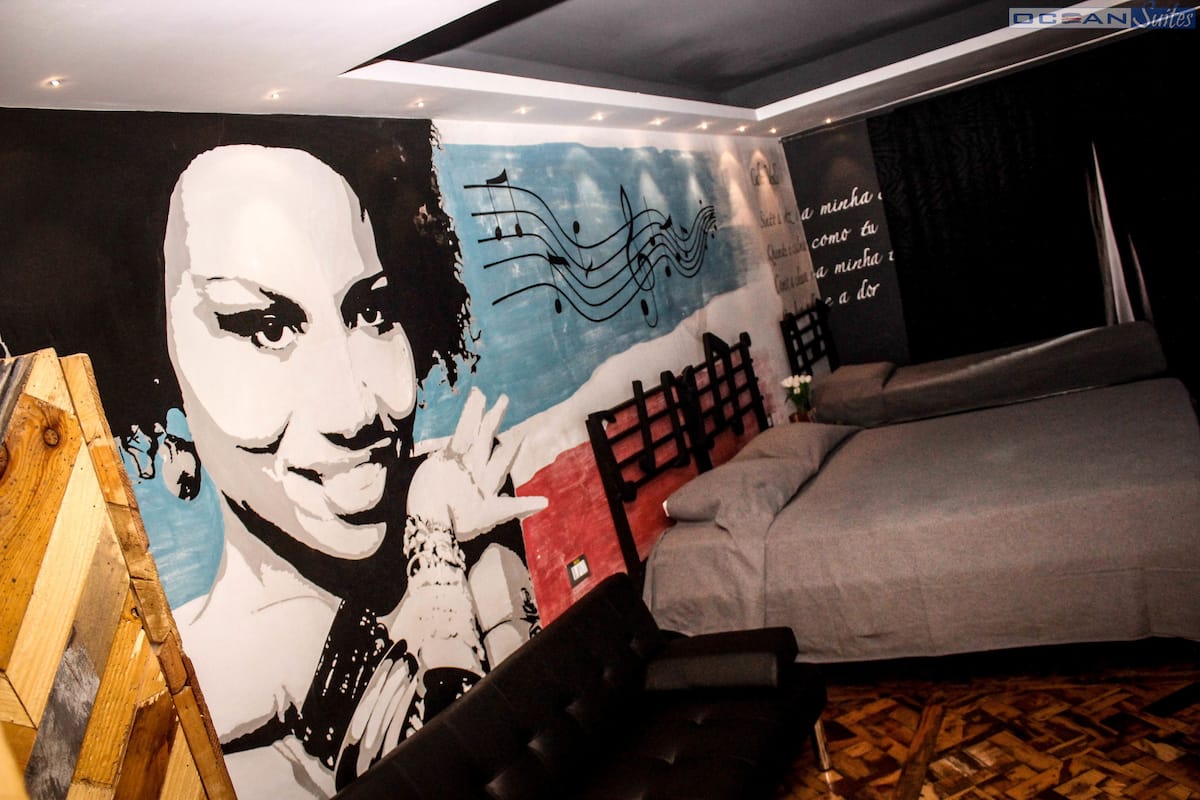 A hotel room with a large mural, a bed, a wooden floor, and a desk.
