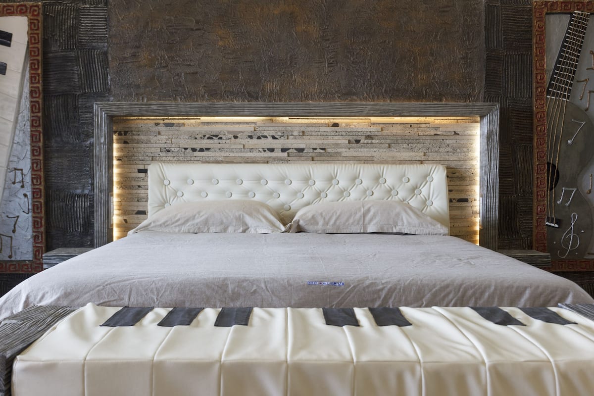 A bed with a tufted headboard and a piano-themed bedspread.