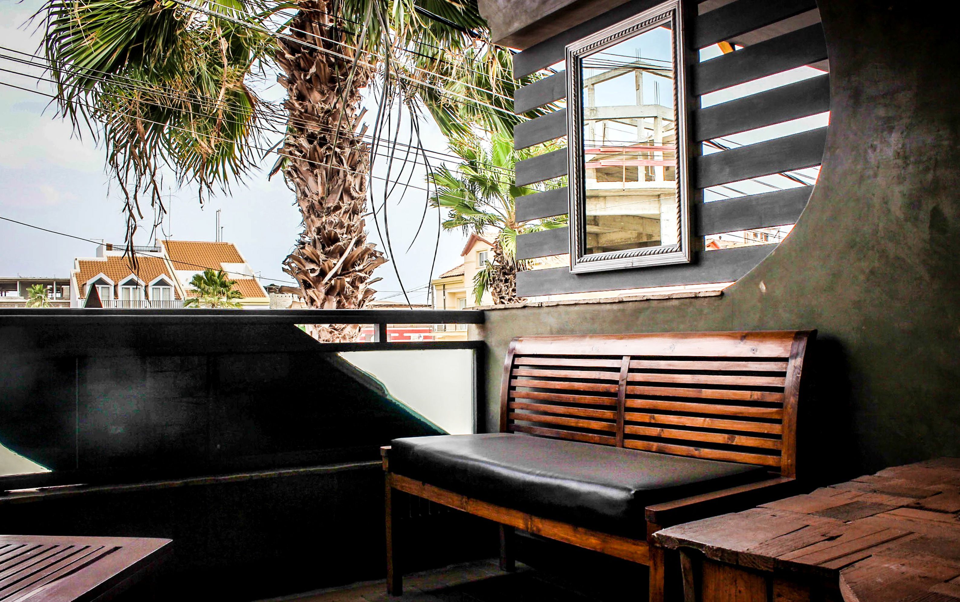 A wooden bench with a cushioned seat, a small table, and a window with a view of buildings and palm trees.