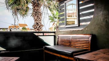 A wooden bench with a cushioned seat, a small table, and a window with a view of buildings and palm trees.